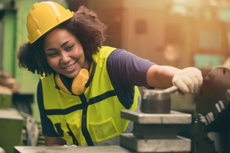 Young woman in hard hat and hi-vis working in a factory