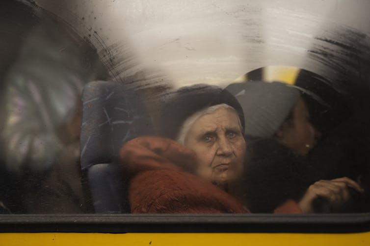 A grey haired woman gazes sadly out a bus window.
