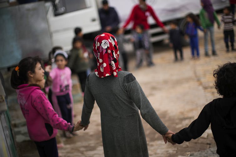 Children and two adults stand in a semi-circle holding hands. One girl wears a Minnie Mouse head scarf.