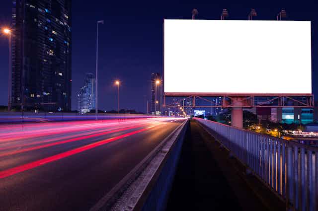 A blank highway billboard at night, with cars speeding by.