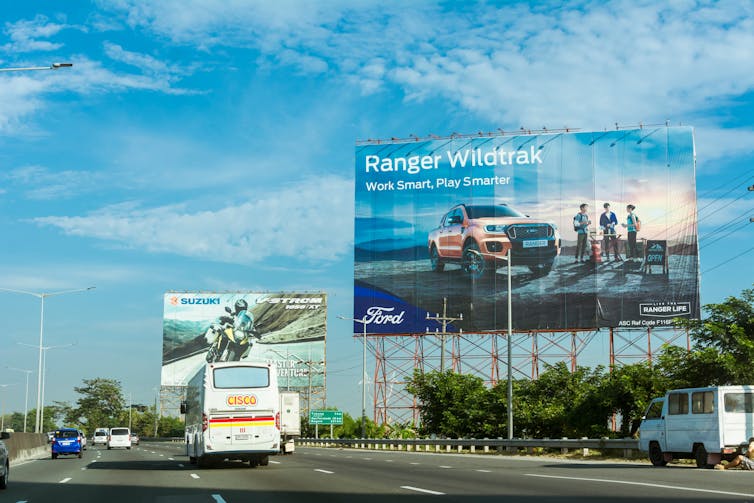 Billboards for motorcycles and pickup trucks line a freeway.
