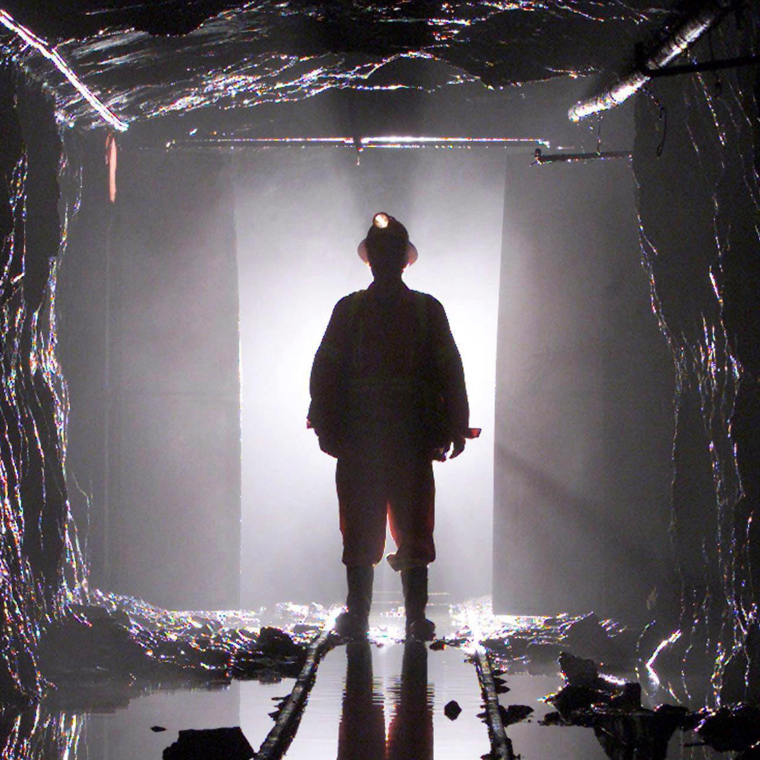 A man stands silhouetted through a door way in a mine shaft, he's wearing a hard hat