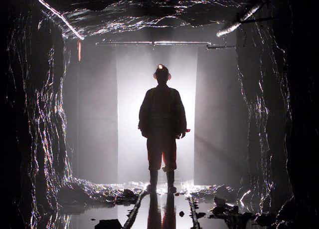 A man stands silhouetted through a door way in a mine shaft, he's wearing a hard hat