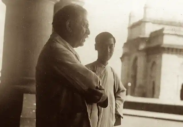 Younger man observes older man whose arms are folded.