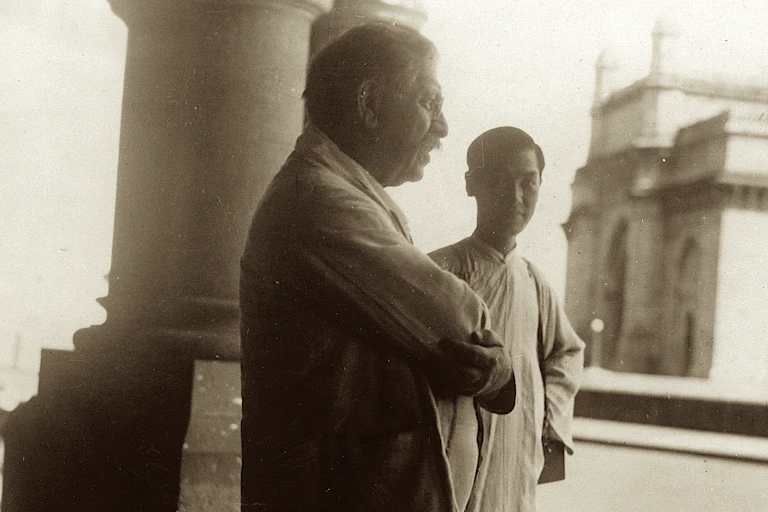 Younger man observes older man whose arms are folded.