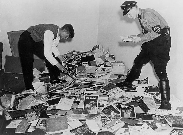 Two men pick through a pile of books.