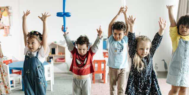 Children seen in a classroom raising their arms.