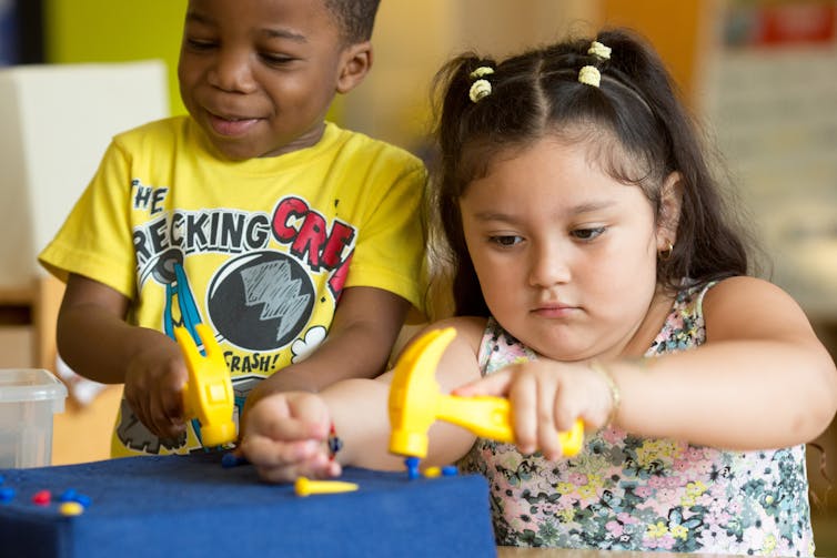 A boy and girl seen playing with play tools in a classroom.