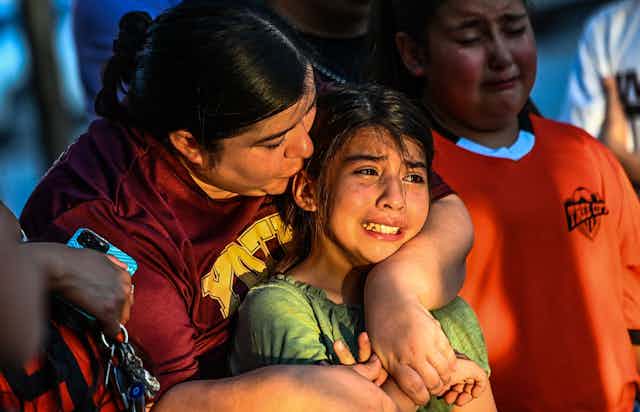 A young girl in tears is comforted an older woman who emvraces her.