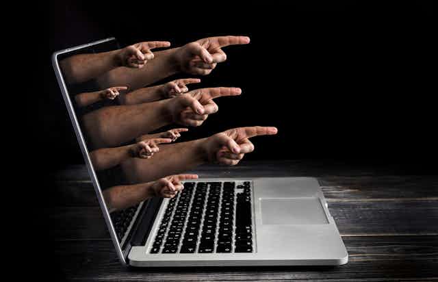 an open laptop with hands with pointing fingers emerging from the screen
