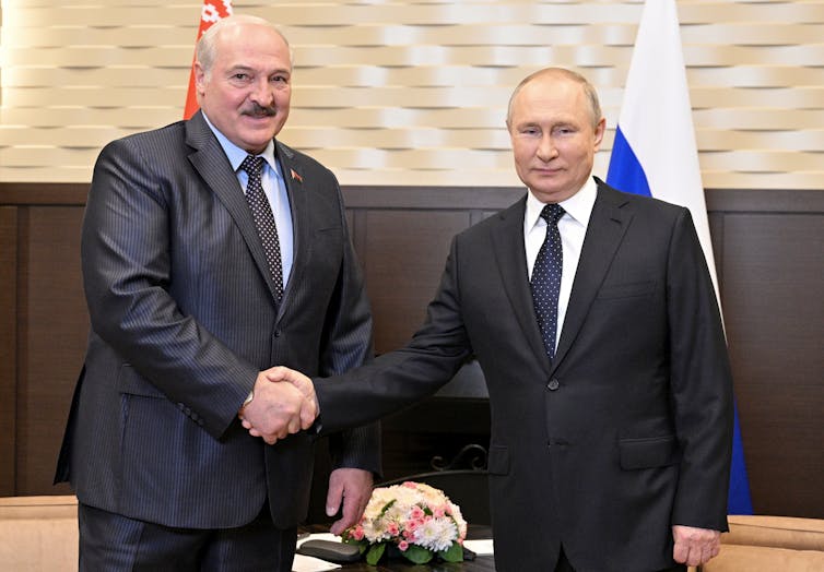 Two balding men, one taller with a moustache, shake hands.