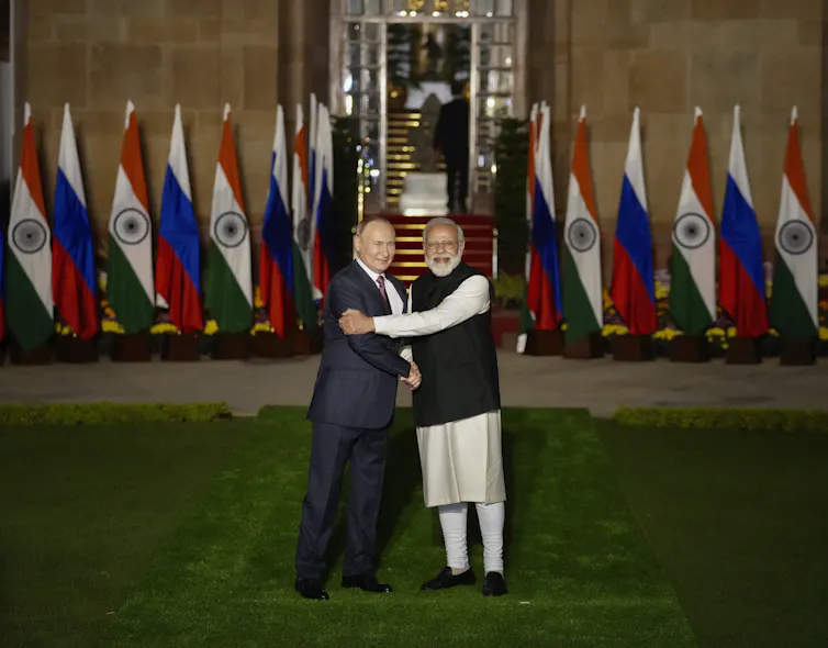 A balding man in a suit is embraced by another man with a white beard.