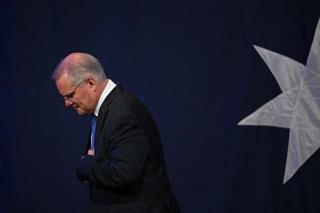 Scott Morrison walking off stage with his arms folded and head down. 