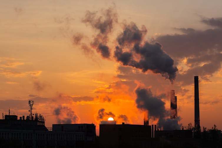 Vista al atardecer del cielo con humo que sale de las chimeneas de los edificios.