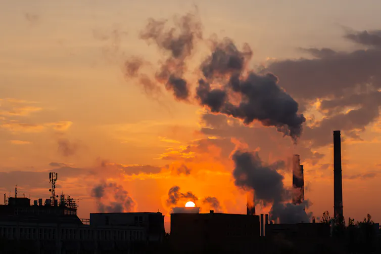 Vista al atardecer del cielo con humo que sale de las chimeneas de los edificios.