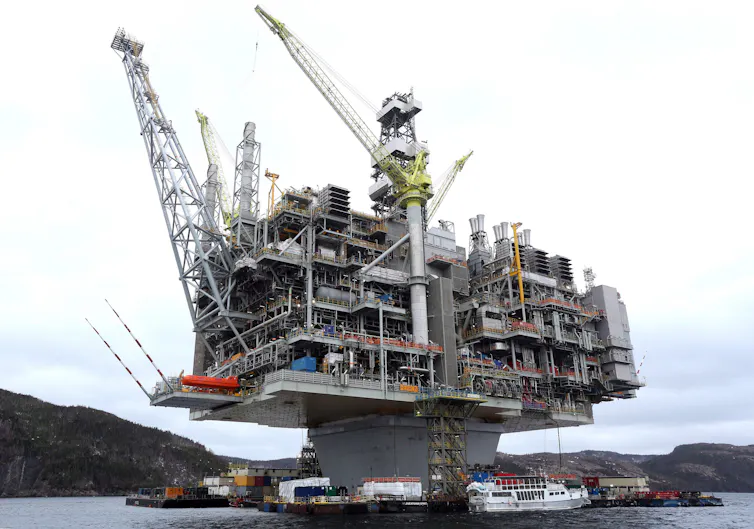 A multi-level oil platform with rocky shoreline behind it.