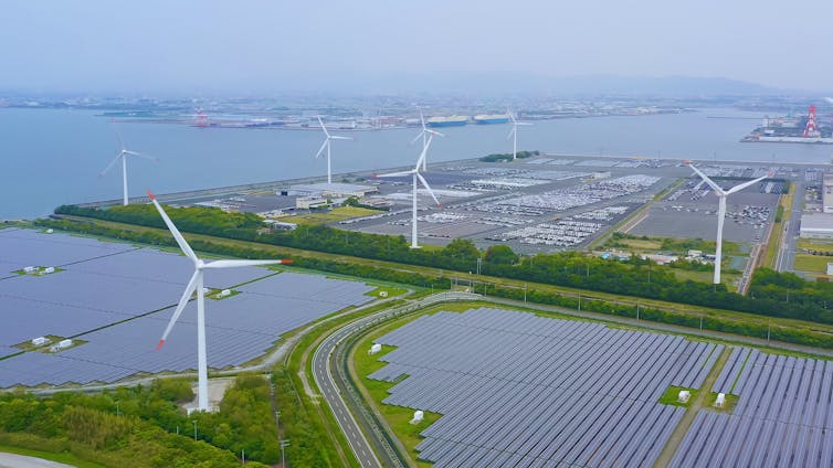 A photoillustration of a conceptualized renewable energy hub with wind turbines and solar panels near a port.