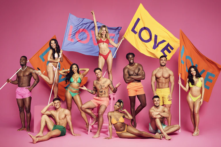The cast of Love Island, 11 attractive young people in neon bikinis and swim trunks, posing with large colourful flags reading LOVE, against a bright pink background