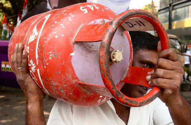 An Indian man carries a red gas canister.