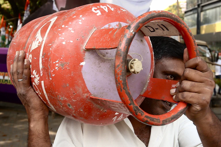 An Indian man carries a red gas canister.