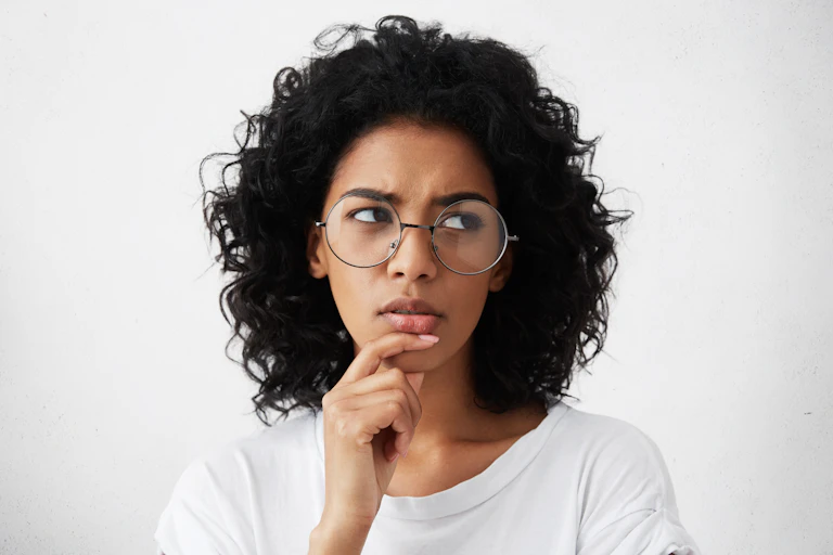 Headshot of dark-haired young woman wearing round glasses, with a thoughtful expression