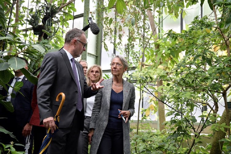 La première ministre discute avec un homme, suivis de plusieurs autres personnes, dans une serre végétalisée.