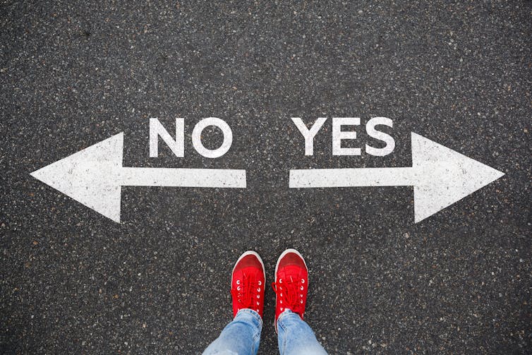 Bird's eye view of red shows and lower legs standing between two arrows, left for no and right for yes