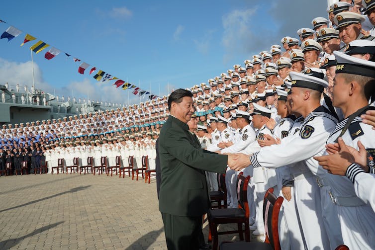 Xi Jinping shakes hand of a sailor from rows of naval personnel.