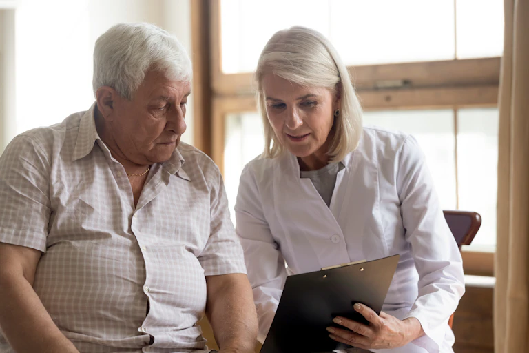 Older man speak with a female doctor. Both are looking at a clipboard the doctor is holding.