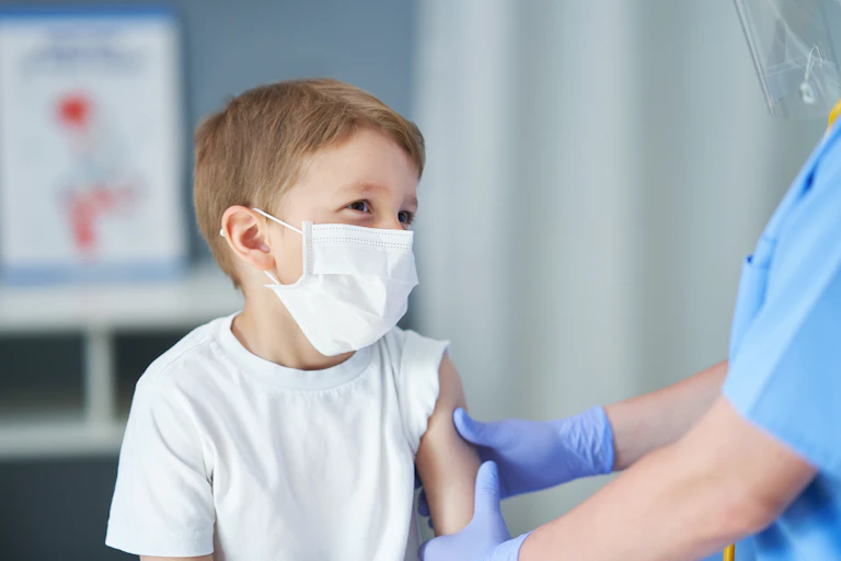 A small boy wearing a face mask, with his sleeve rolled up.
