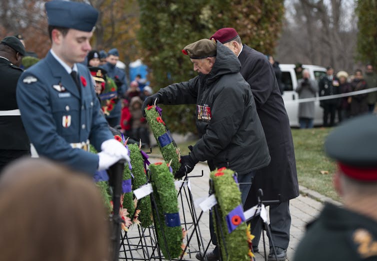 A man lays a wreath in a park with the assistance of another man