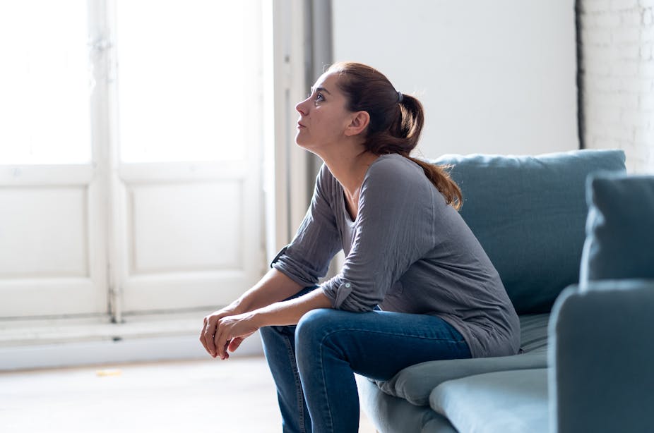 Young woman with long brown hair in a ponytail sits on a sofa and stares into the distance