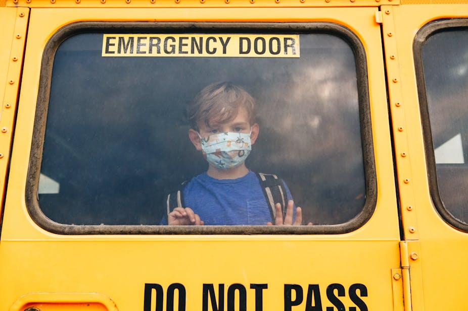 A young schoolboy peers out the window of an emergency door of a yellow school bus.