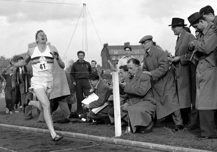 A black and white photo shows a man crossing a finish line