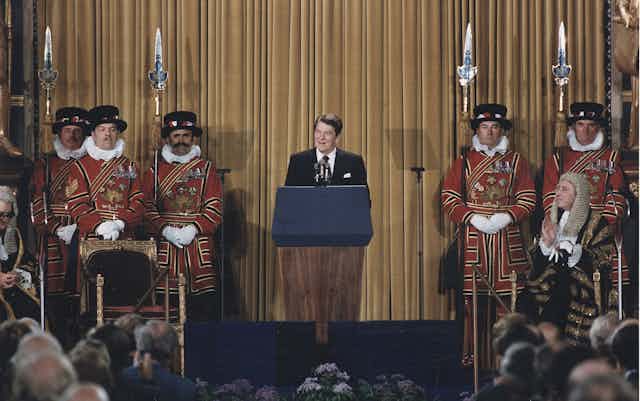 President Reagan addressing British Parliament, standing at a podium with Beefeaters, ceremonial guards, on either side of him