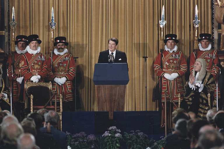 President Reagan addressing British Parliament, standing at a podium with Beefeaters, ceremonial guards, on either side of him