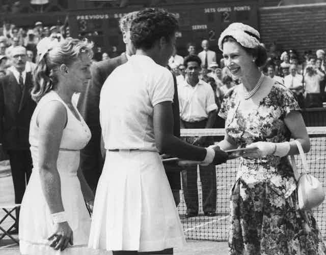 Queen Elizabeth shakes hands with a woman on a tennis court.