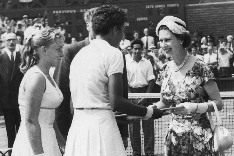 Queen Elizabeth shakes hands with a woman on a tennis court.