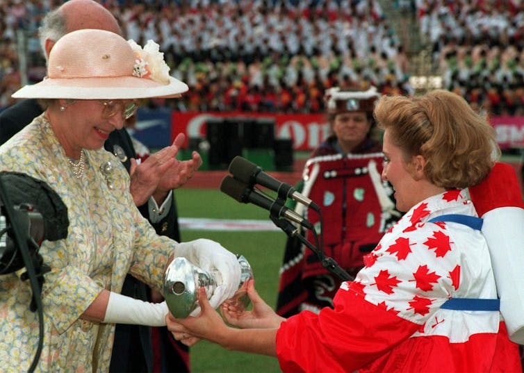 A woman receives a baton from another woman dressed head to toe in Canadian flags