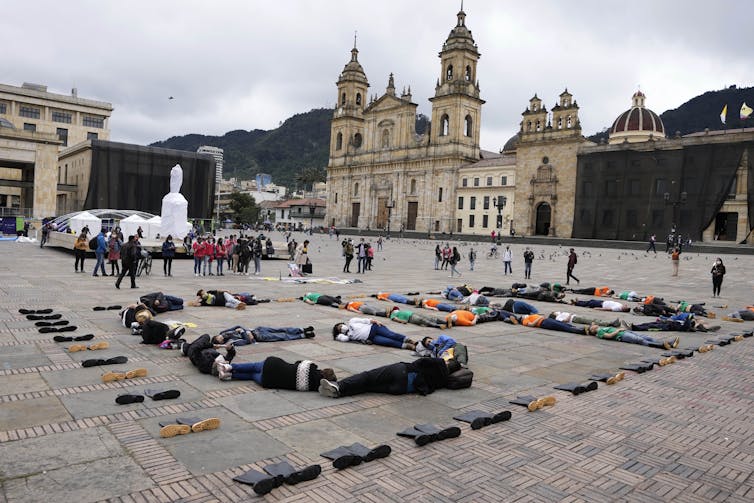 Protesters lie on the ground in a city square, with government buildings in the background.