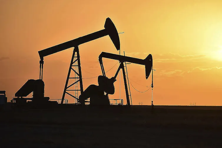 Two oil pumps silhouetted against the sky as the sun sets