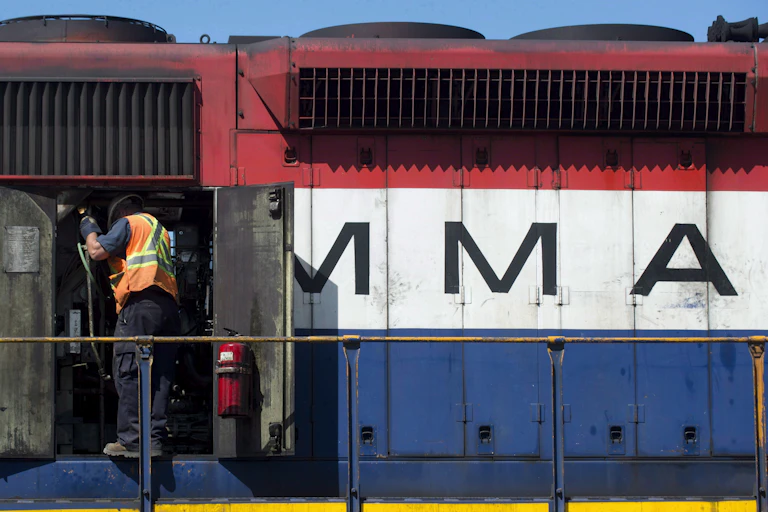 A train engineer in a construction vest standing in the open doors of a train