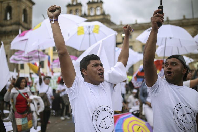 Two men in white T-shirts raise their arms in celebration.