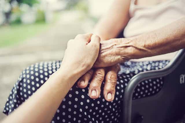 une personne tient la main d'une femme âgée dans un fauteuil roulant