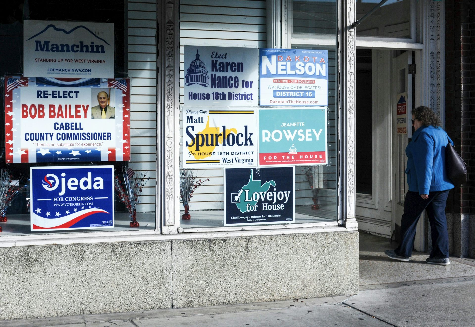 Tall windows of a commercial building plastered with campaign posters in many colors.