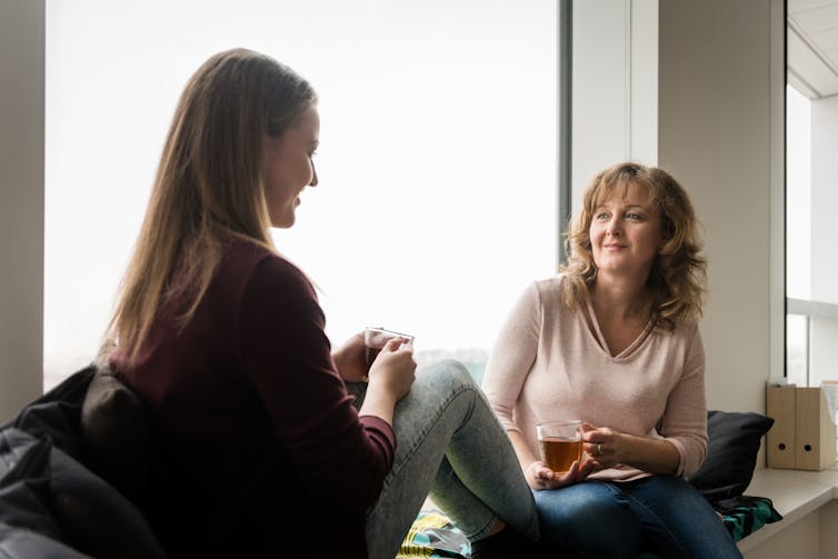 woman and teenager sit on window sill and chat