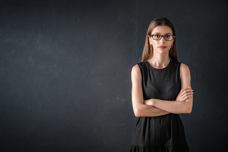A woman with her arms folded stands in front of a black chalkboard.