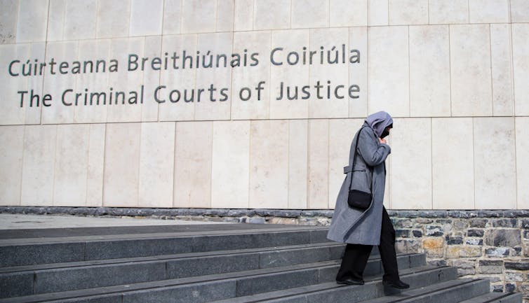 A woman in black trousers and a grey headscarf walks down stone steps next to a court.