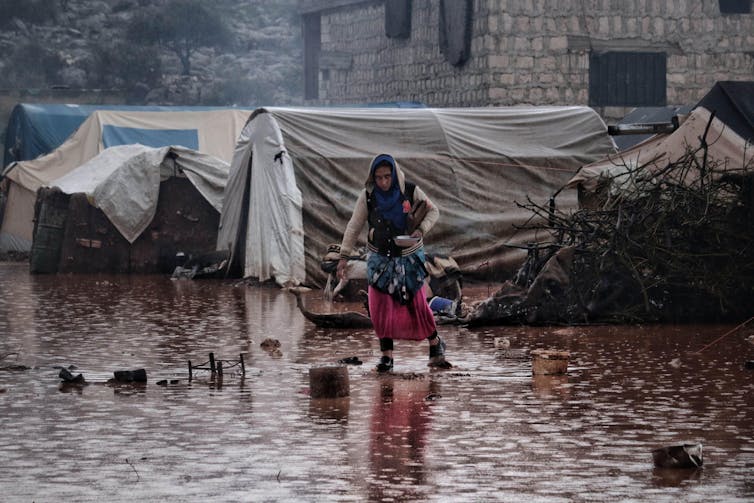 A woman walks through a camp of tents that has been flooded.