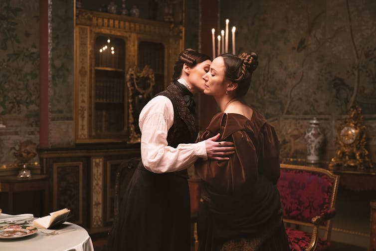 Two women in period dress kiss.